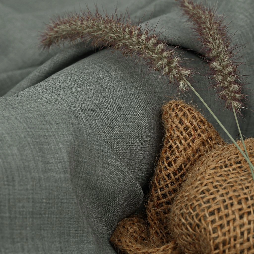 A close-up of the SilentShell softshell fabric, lichen green with a fine knit backing, slightly rumpled on a bone-colored surface.